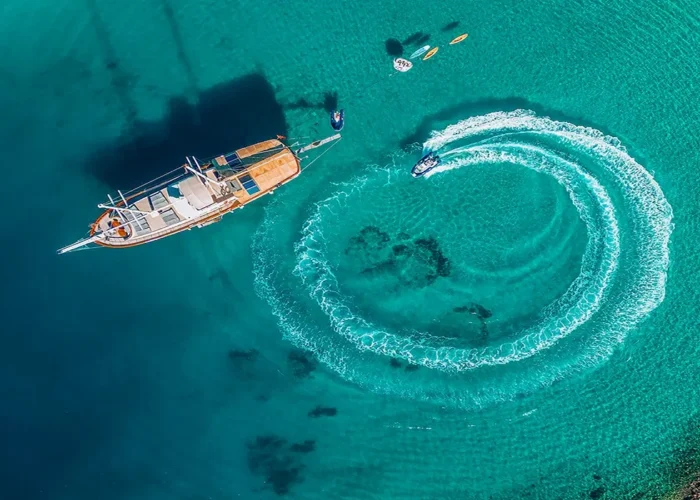 Aerial view of a gulet and jet ski creating circular waves on turquoise waters during a Blue Cruise Turkey adventure