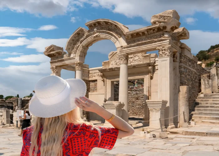 Visitor looking at ancient marble gate ruins in Ephesus with white hat and red dress
