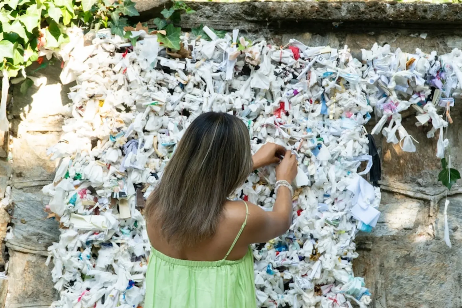 Woman tying wish ribbons on ancient stone wall in House of Virgin Mary