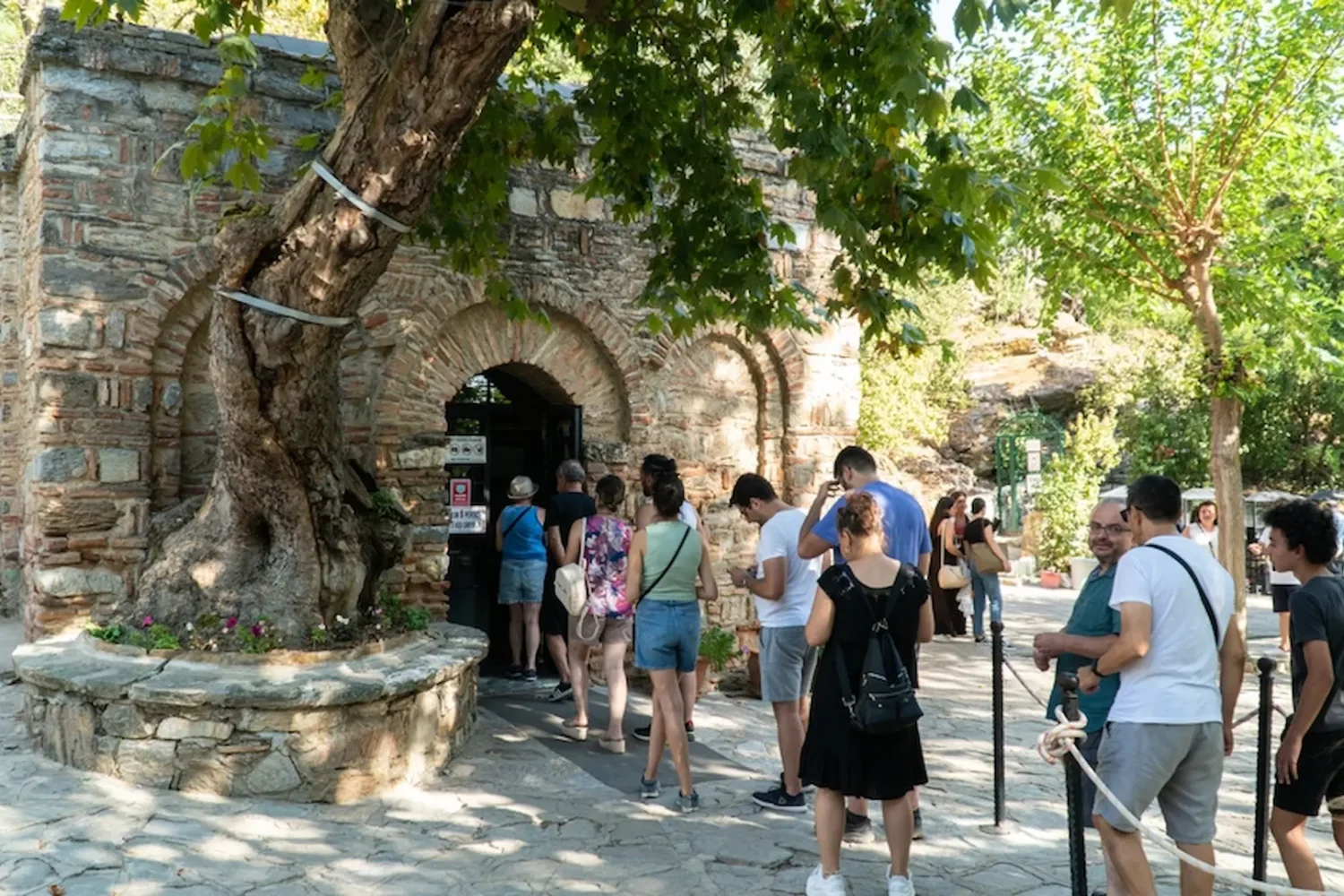 Line of tourists entering a rustic stone arch building among trees in Virgin Mary House