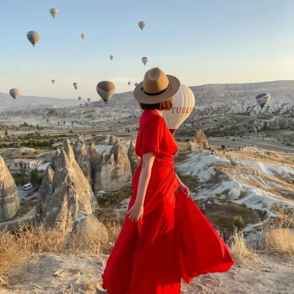 Woman in red dress watching hot air balloons over Cappadocia at sunrise