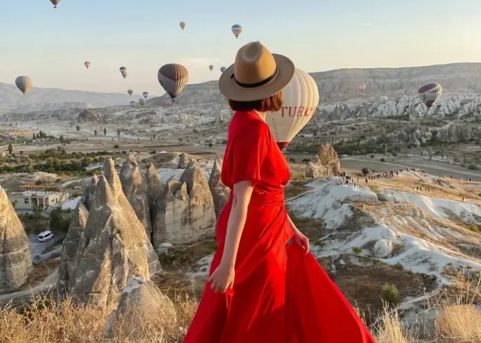 Woman in red dress watching hot air balloons over Cappadocia at sunrise